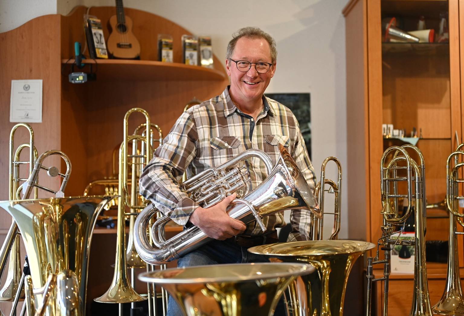Thorsten Steinhaus mit einem Euphonium in seinem Musikhaus, umgeben von Posaunen und Tuben